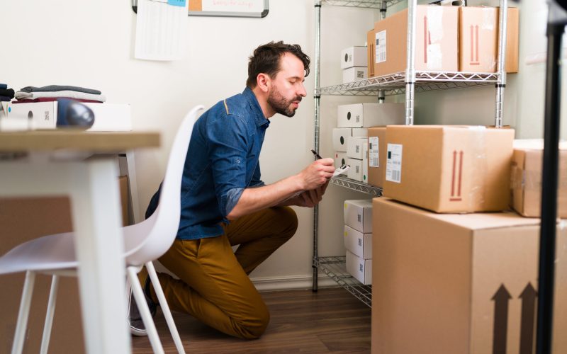 Checking that all the packages are in order. Handsome man writing on a clipboard the customers' information to ship their online purchases